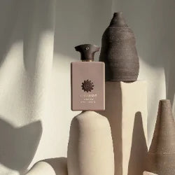 Amouage Opus XIV Royal Tobacco Eau de Parfum bottle styled among sculptural ceramic vessels in warm, natural light.