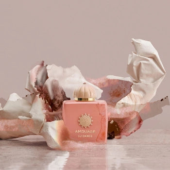 Pink Amouage perfume bottle with decorative elements on a light background