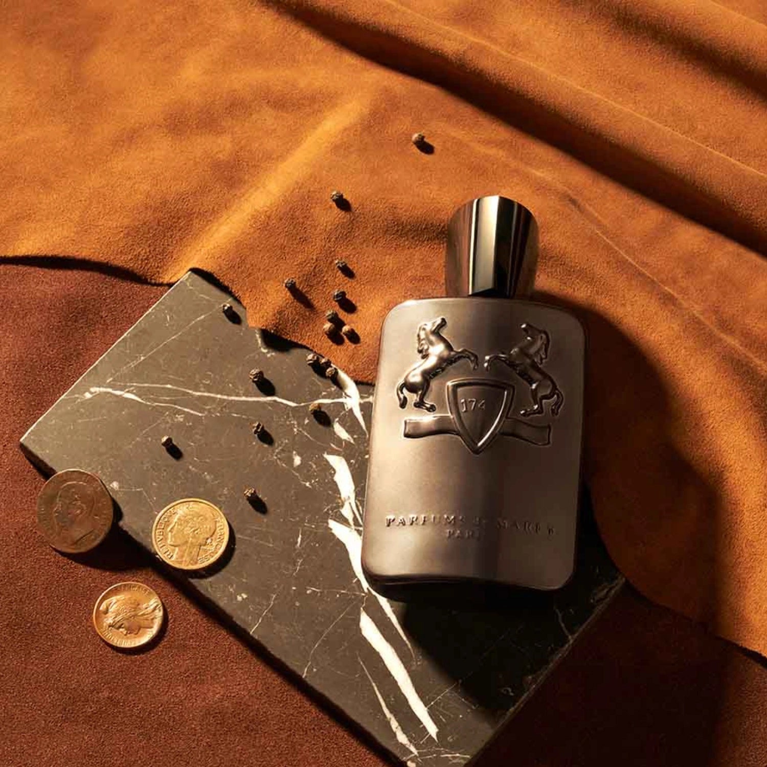 Parfums de Marly Herod Eau de Parfum bottle with a matte dark brown finish and matching dark brown cap displayed on a black marble slab with coffee beans and gold coins.