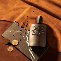 Parfums de Marly Herod Eau de Parfum bottle with a matte dark brown finish and matching dark brown cap displayed on a black marble slab with coffee beans and gold coins.