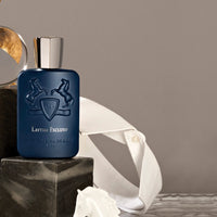 Parfums de Marly Layton Exclusif Eau de Parfum bottle in deep matte midnight-blue with an embossed horse crest and silver cap displayed on black marble blocks beside a crisp white dress shirt, creating a refined luxury setting.